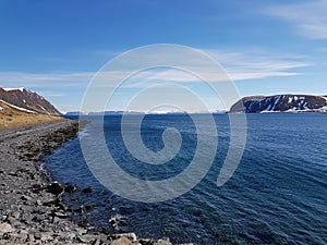 Snowy mountain peaks in early spring with clear blue sky and sunshine reflection on fjord surface