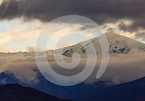 A snowy mountain surrounded by white and dark clouds