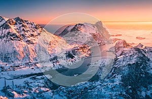 Snowy mountains, blue sea and sky with golden sunlight. Aerial