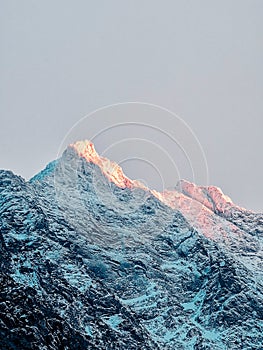 Snowy mountains with rays of the sun on the background of a gray sky