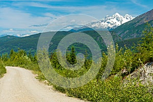 Snowy mountains tower over a dirt road near Usk, British Columbia, Canada