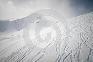 Snowy off-piste ski slope with ski and snowboard tracks on a sunny winter day. Freeride in high mountains