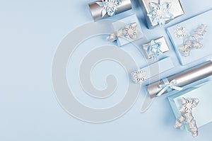 Snowy pastel blue christmas background of silver gift boxes and sparkles christmas tree, snowflakes with copy space, top view.