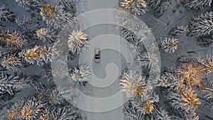 Snowy road with car surrounded by snowcovered trees viewed from above