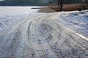 Snowy road next to a frozen icy lake.