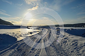 Snowy road with tromsoe city island in the background at sunrise