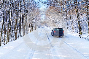 Snowy road in winter forest with single car