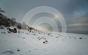 snowy rocky shore of the lake on background gray cloudy sky