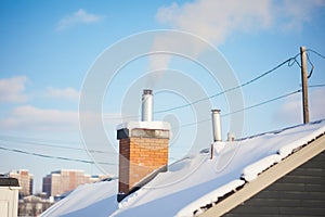 snowy rooftop with chimney, smoke against clear blue sky