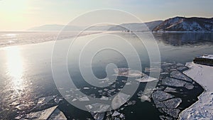 A snowy shoreline next to a frozen lake seen from an aerial view