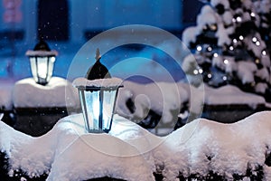 snowy street lamps in night city with fir-tree and christmas lights in background