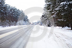 Snowy street surrounded by pine trees, winter road in the forest. Freezing day