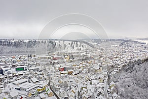 Snowy winter aerial with a view over a white snow covered city framed by hills.