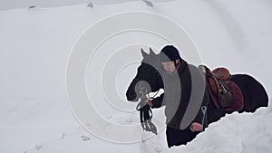 Snowy winter, disabled man jockey leads, holding with reins a black horse on the way. man has a prosthesis instead of