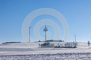 snowy winter landscape with a field, forest, radio tower and wind turbines for power generation