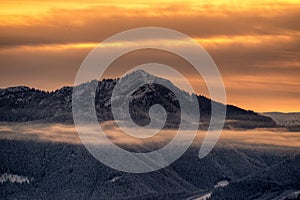 Zasněžená zimní horská krajina a barevná obloha kvůli východu slunce nad kopcem Sina v pohoří Nízké Tatry na Slovensku