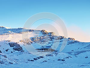 Snowy winter mountain and old stony cottage in small valley bellow peak. Clear blue sky.