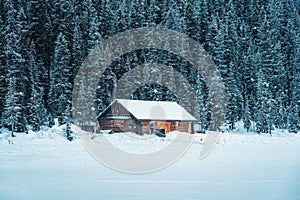 Snowy wooden cottage glowing in pine forest on Lake Louise in wintertime at Banff national park