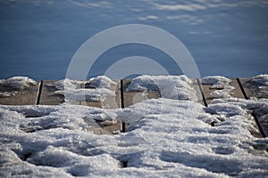 Snowy wooden pier boards and blue unfrozen river water