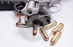 A snub nosed, stainless 357 magnum revolver on top of a black 9mm pistol with four bullets each caliber in front of them