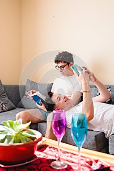 Snuggling latin gay couple in pajama sharing their hobbies on sofa on day off.