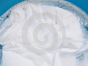 soak white T-shirt in detergent solution, laundry cloth cleaning with washing powder in tub photo