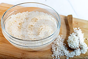 Soaked rice, grain, cloudy liquid water in glass bowl on wooden background