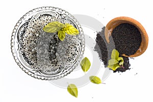Soaked sweet basil or tukhmaria or falooda seeds or sabja seeds in a bowl with raw sweet basil seed isolated on white with a mint