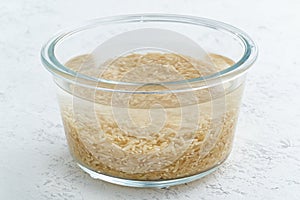 Soaking brown rice cereal in water to ferment cereals and neutralize phytic acid. Large glass bowl with grains flooded with water
