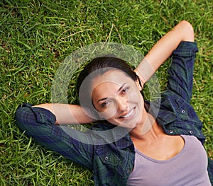 Soaking up the tranquility. High angle portrait of an attractive young woman lying on the grass.