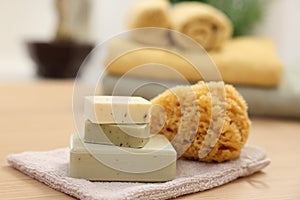 Soap bars and natural sponge on light wooden table, closeup. Spa therapy