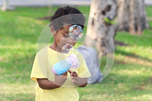 Soap bubble in blued green background, happy African boy making bubbles with blowing bubble gun toy in garden. Kid spends time