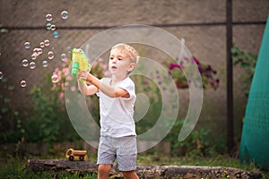 Soap Bubble Games. The boy in the backyard is playing with a water gun. Boy in summer playing with water and soap bubbles close-up