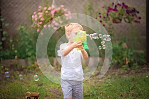 Soap Bubble Games. The boy in the backyard is playing with a water gun. Boy in summer playing with water and soap bubbles close-up