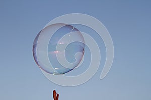 a soap bubble rises in the blue sky and tries to be apprehended with the fingertips of one hand photo