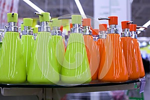 Soap dish dispenser for liquid soap, bathroom ceramic accessories in green and orange colors on glass shelve in store close up