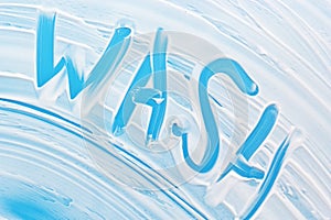 Soap foam on blue background with handwritten word wash. Cleanliness, hygiene, sanitation, disinfection concept