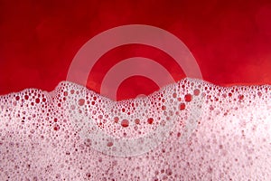 Soap foam with bubbles on a blurred red background. Closeup