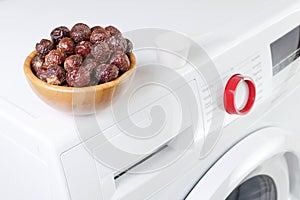 Soap nuts in a bowl on the washing machine and detergent powder, selective focus