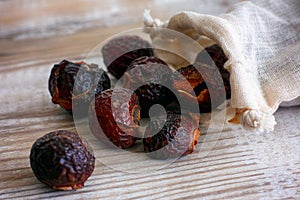 Soap nuts spilling from bag on wooden background.