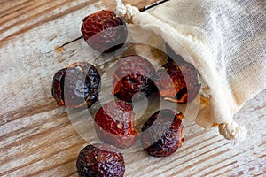 Soap nuts spilling from textile bag on wooden background