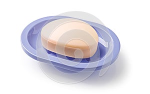 Soap on a soap dish isolated on a white background. Oval shaped beige soap bar in a violet blue plastic soapbox for bathroom and