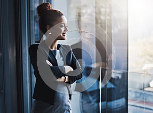 Soaring high in the corporate world. a young businesswoman looking out the window in an office.