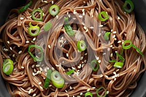 Soba noodles, buckwheat on a black bowl, with spring onion and sesame seeds. Traditional Japanese food.