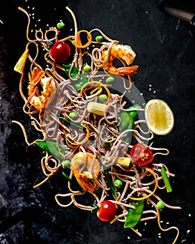 Soba noodles with vegetables and shrimps on black background, top view