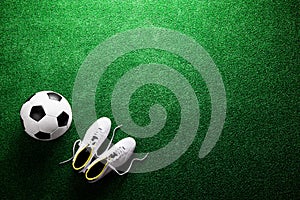 Soccer ball and cleats against green artificial turf, studio sho