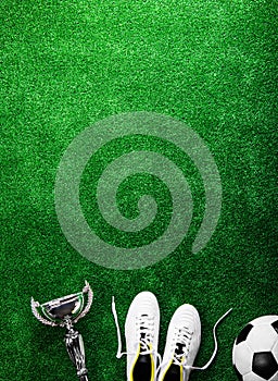 Soccer ball, cleats and trophy against green artificial turf