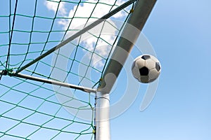 Soccer ball flying into football goal net over sky