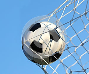 Soccer ball in goal net over blue sky. Football.