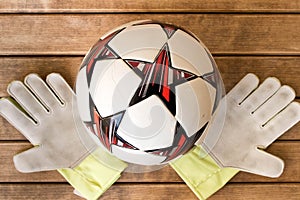 Soccer ball and goalie gloves on wooden background